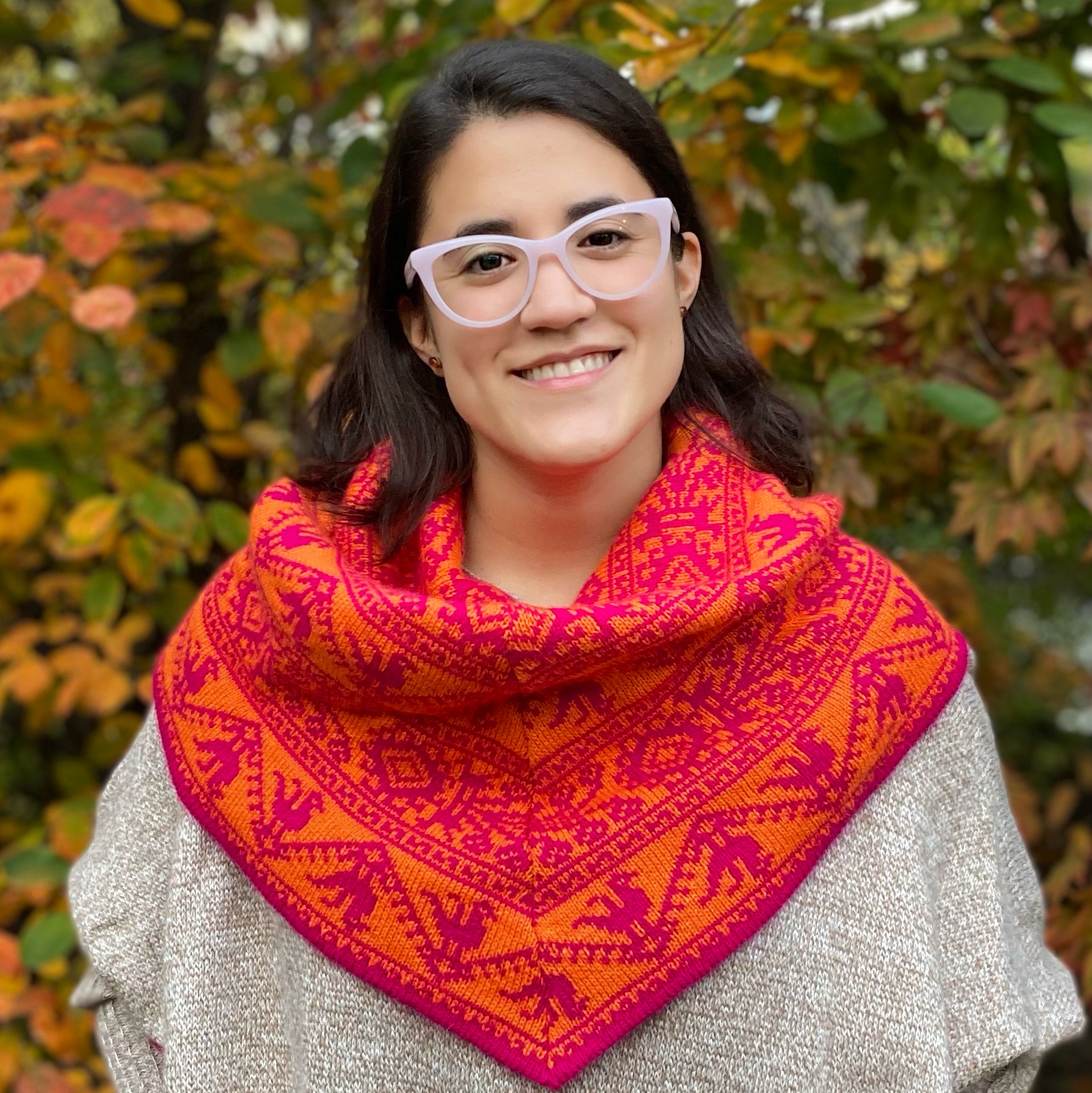 Andrea Román Alfaro in front of yellow and green leaves. There is a red and orange patterned scarf covering Andrea's shoulders and neck.